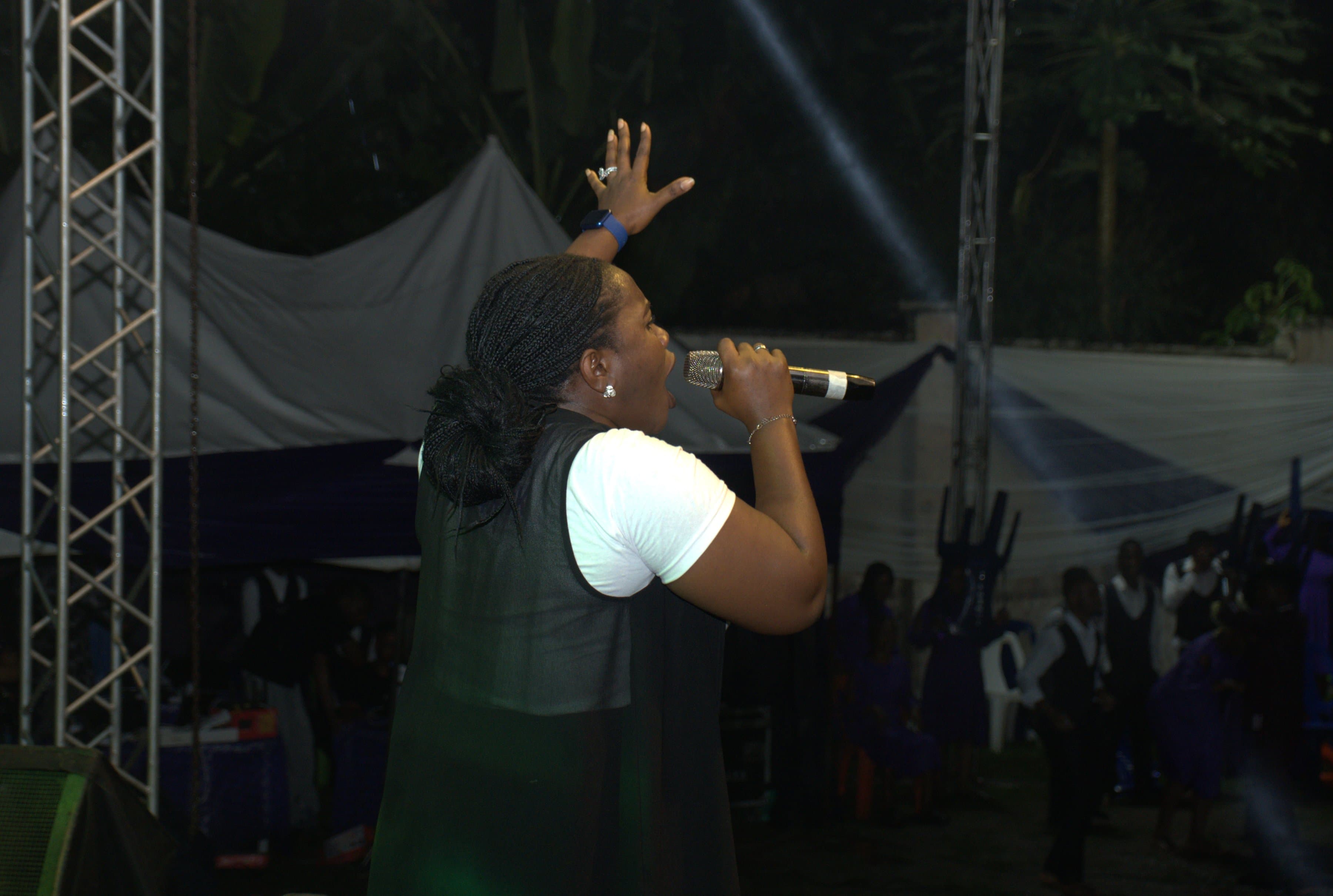 A worshipper singing with a hand raised, stage lights and rigging behind her.