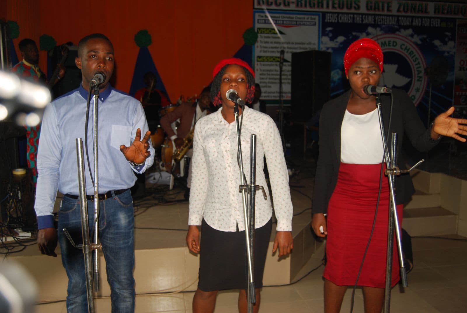 A trio singing together in front of the church banner.
