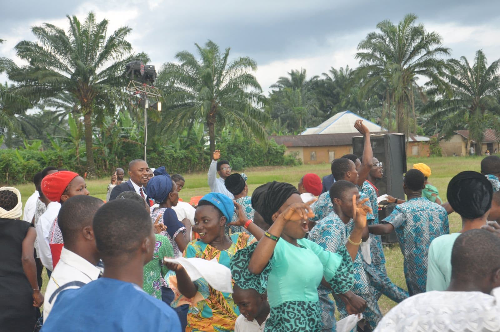 The congregation worshipping outdoors in daylight, palm trees behind.