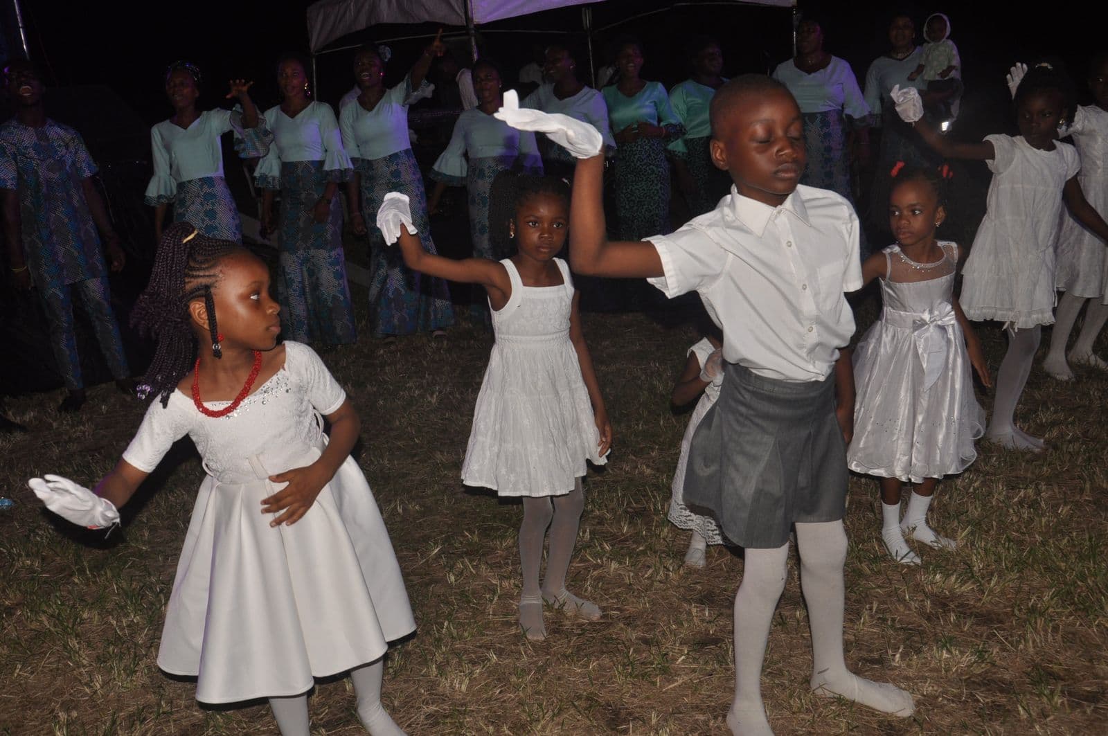 Children dancing at dusk as the stage lights come up behind them.