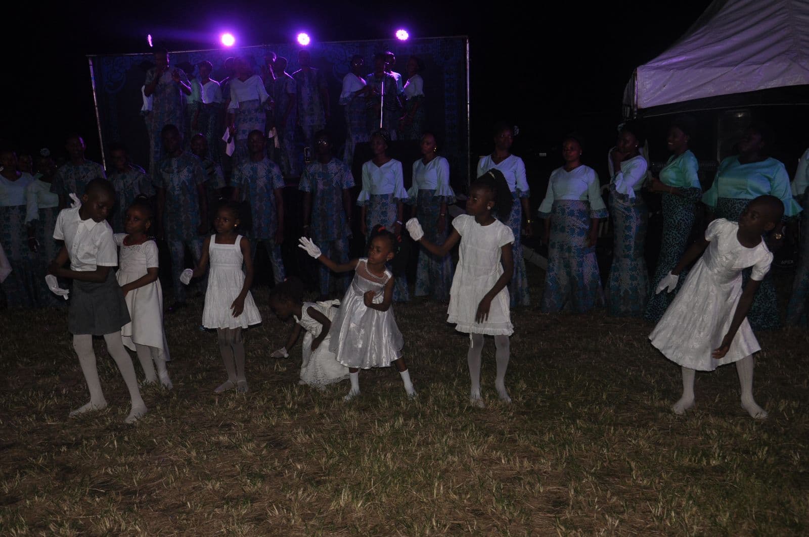 The full choir performing on stage at night under purple light.
