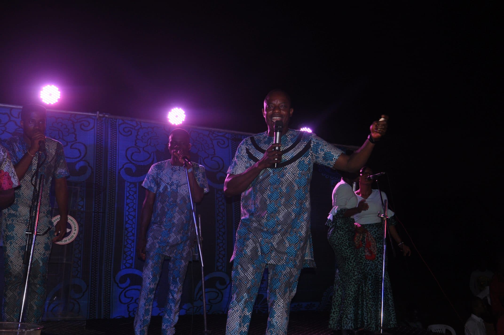 A minister singing under purple stage light at night.