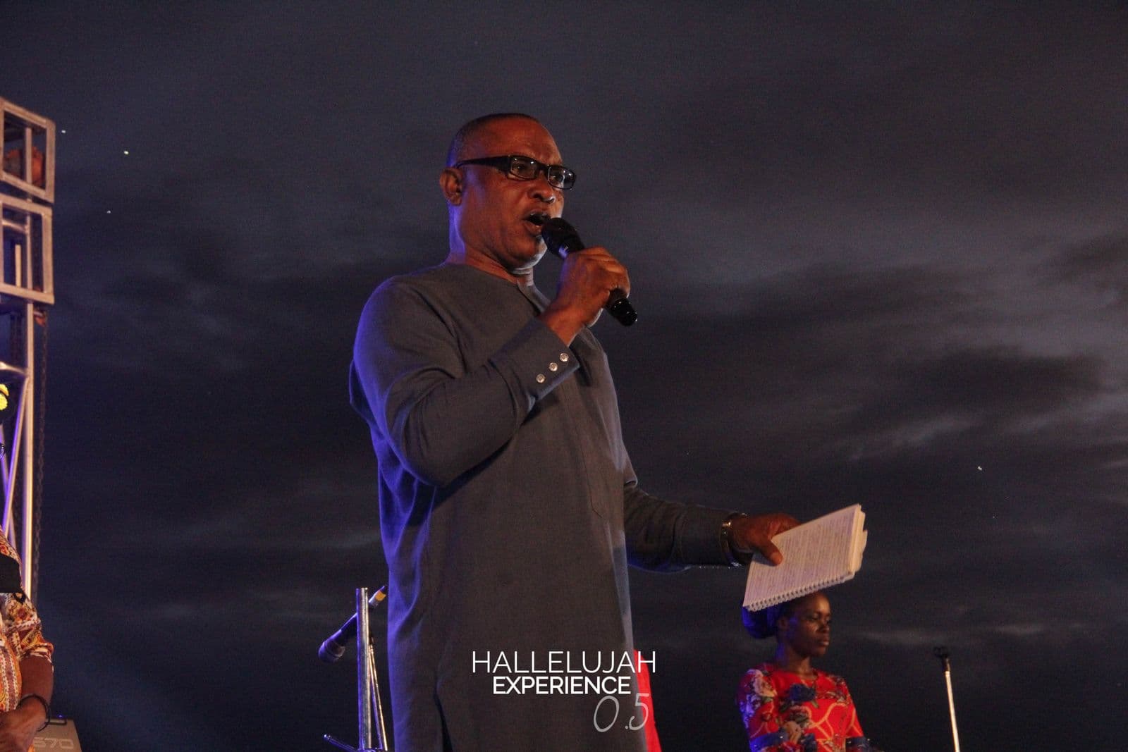 A minister speaking at dusk, the stage rig silhouetted against the sky.