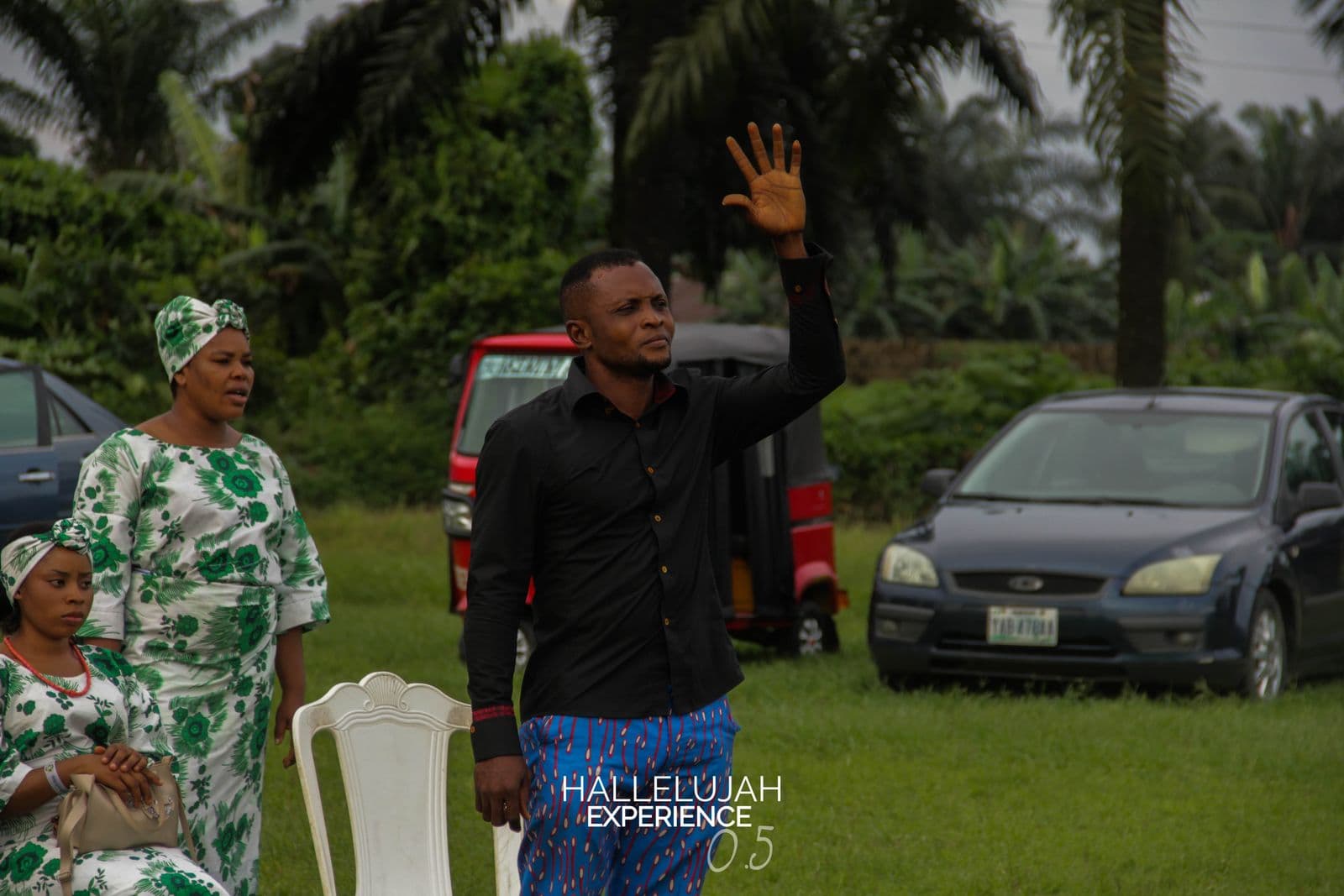 A worshipper with a hand raised, daylight, palm trees behind.