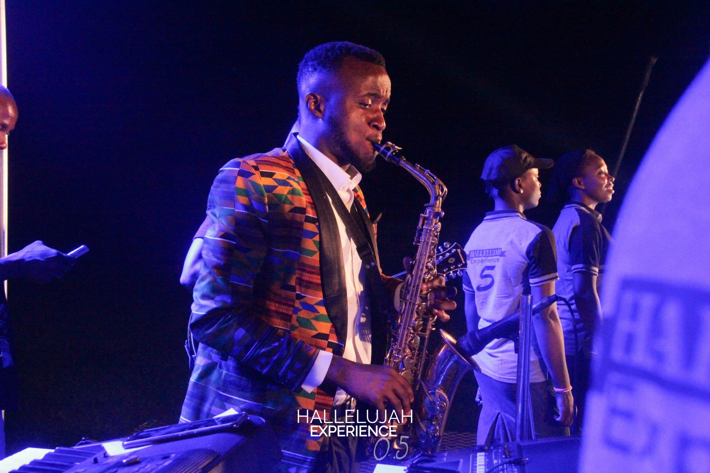 A saxophonist performing under purple stage light.