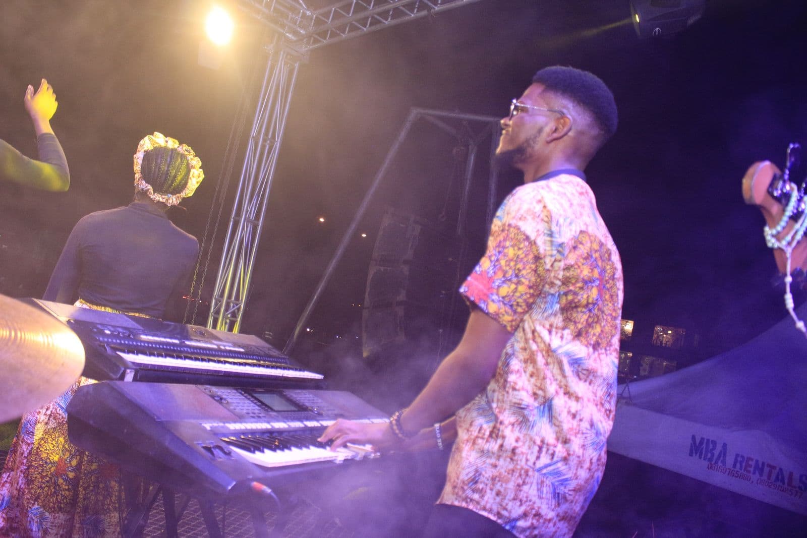 A keyboardist performing under purple and gold light.