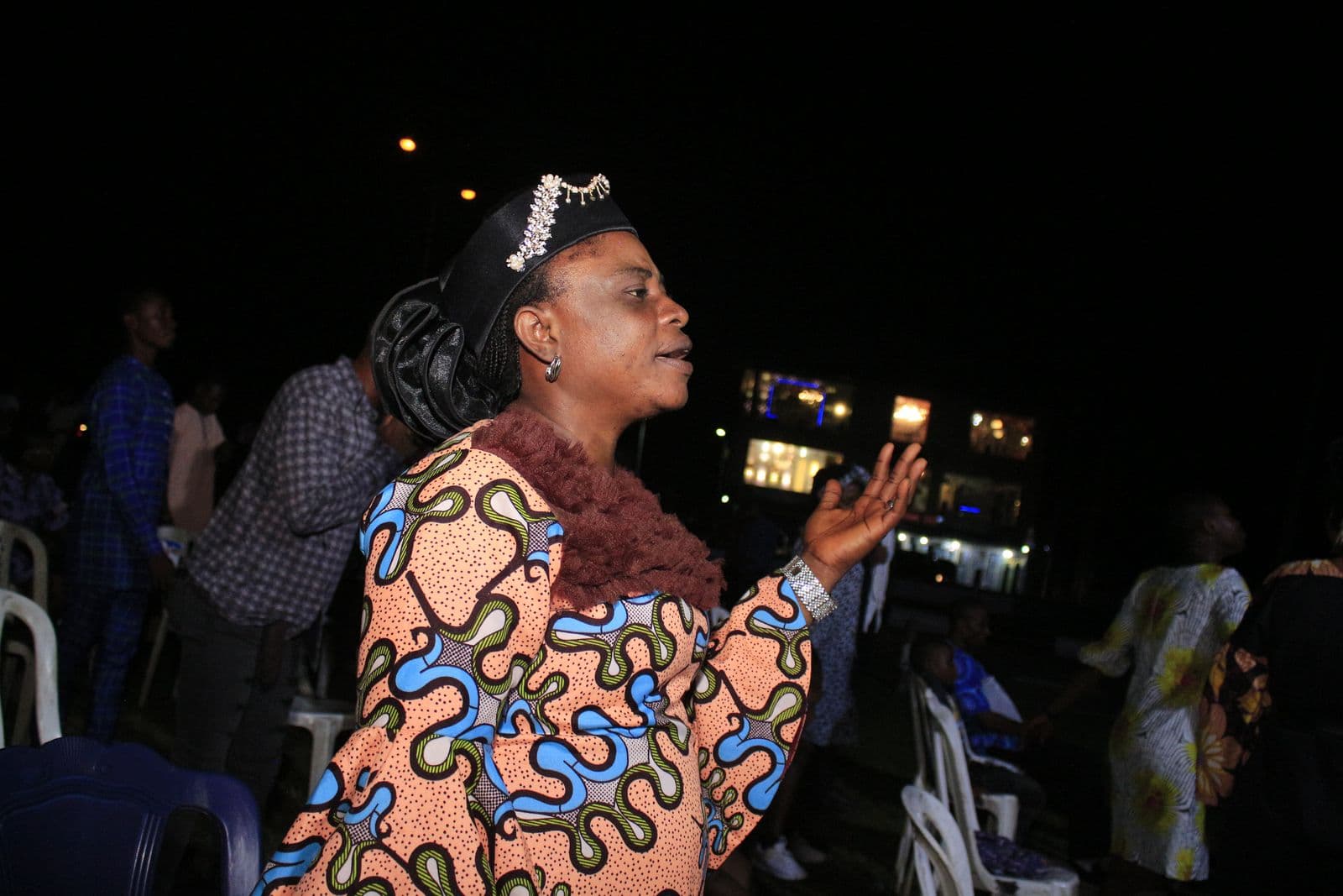 A worshipper with a hand raised at night, tents lit behind her.