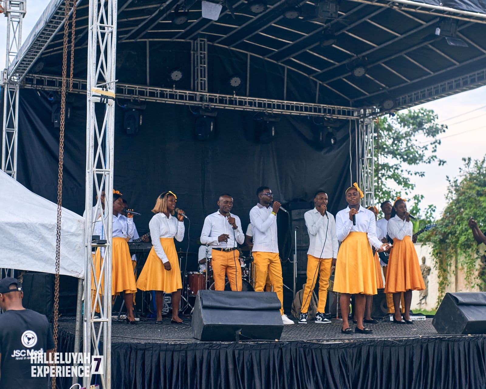 The full choir on stage in matching gold and white, daylight.