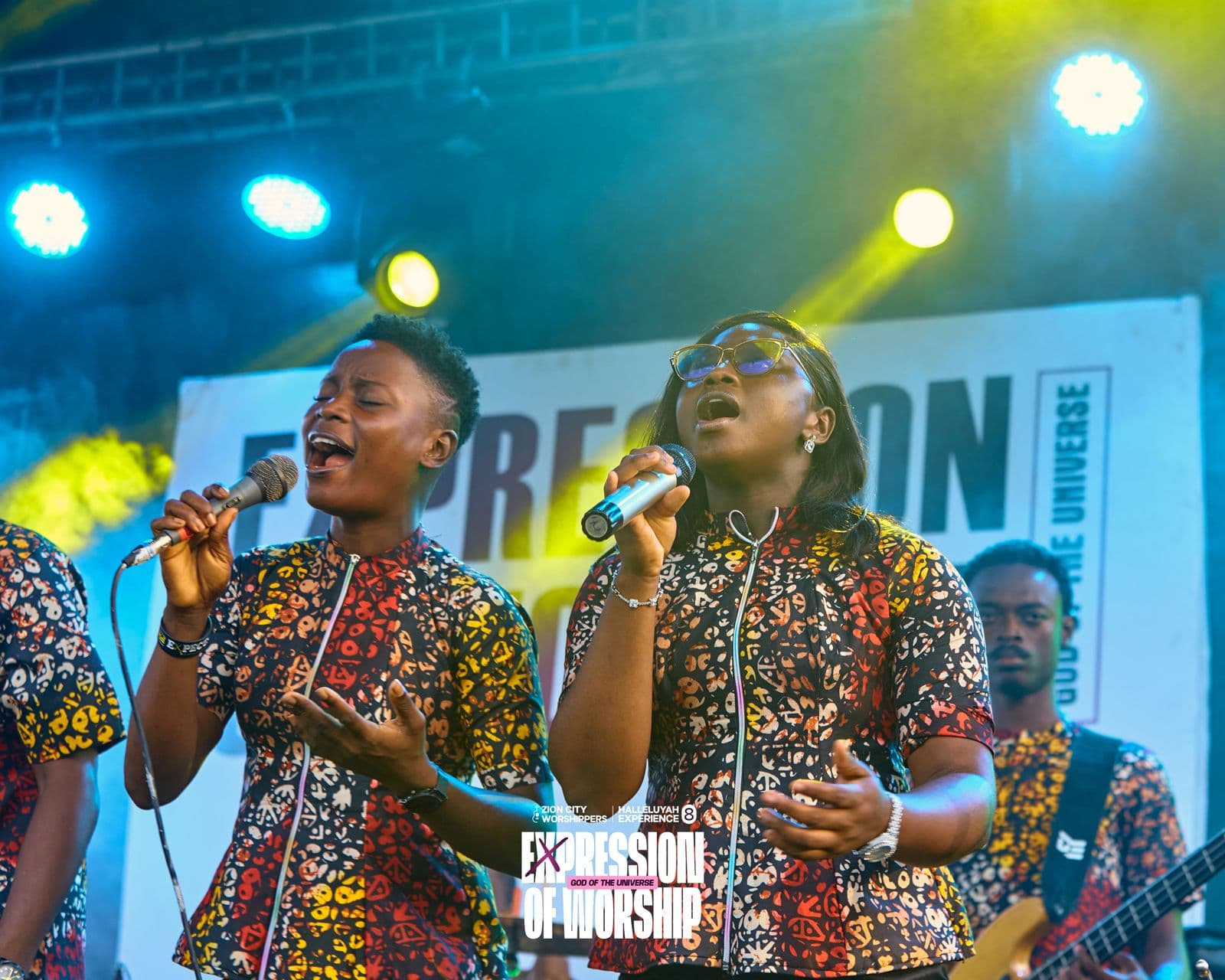 Two vocalists singing together, the stage backdrop visible behind them.