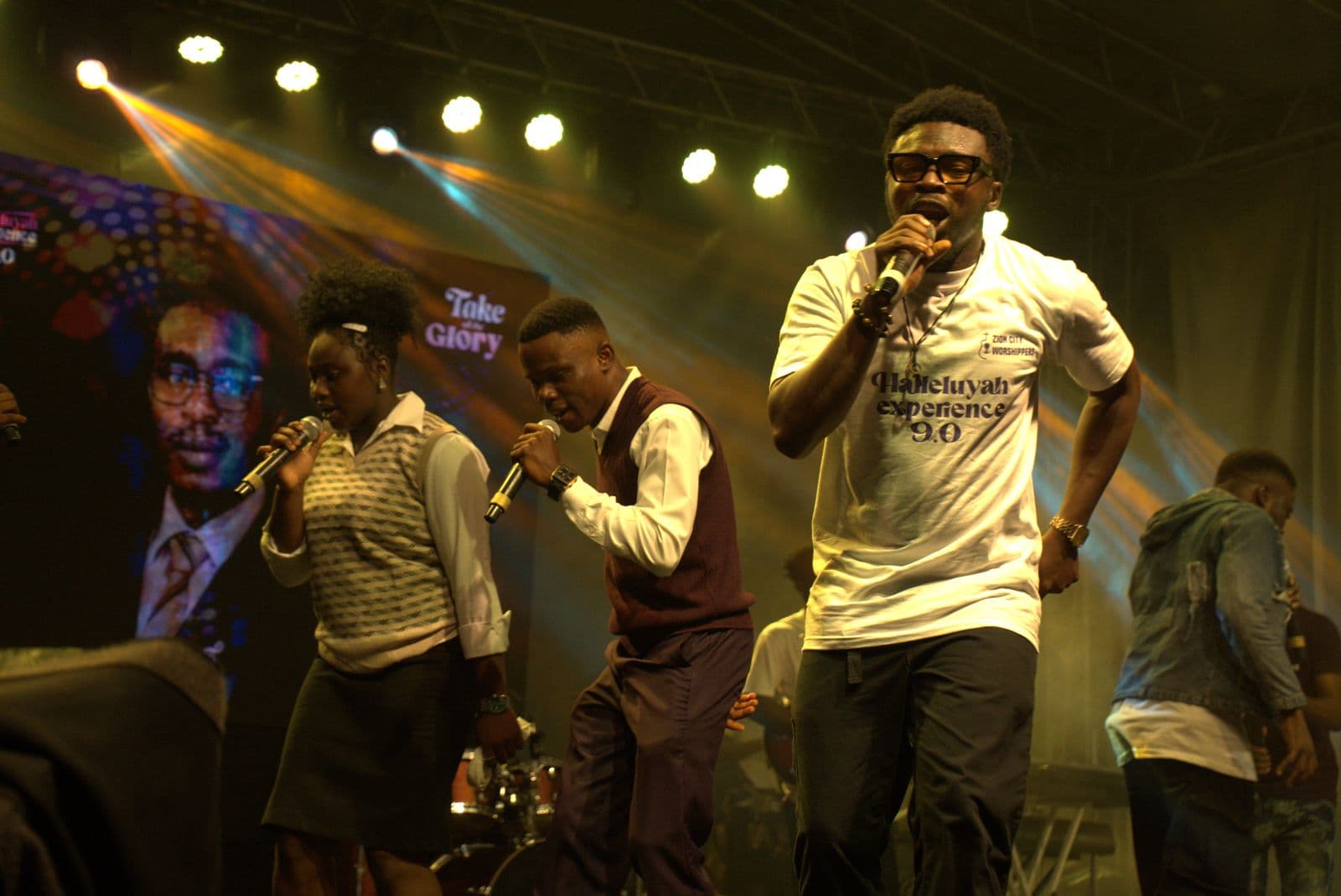 Vocalists singing beneath the "Take All Glory" backdrop.