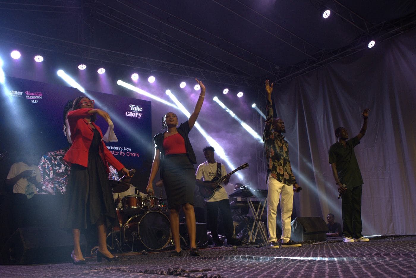 A soloist singing beneath the "Take all the Glory" backdrop.