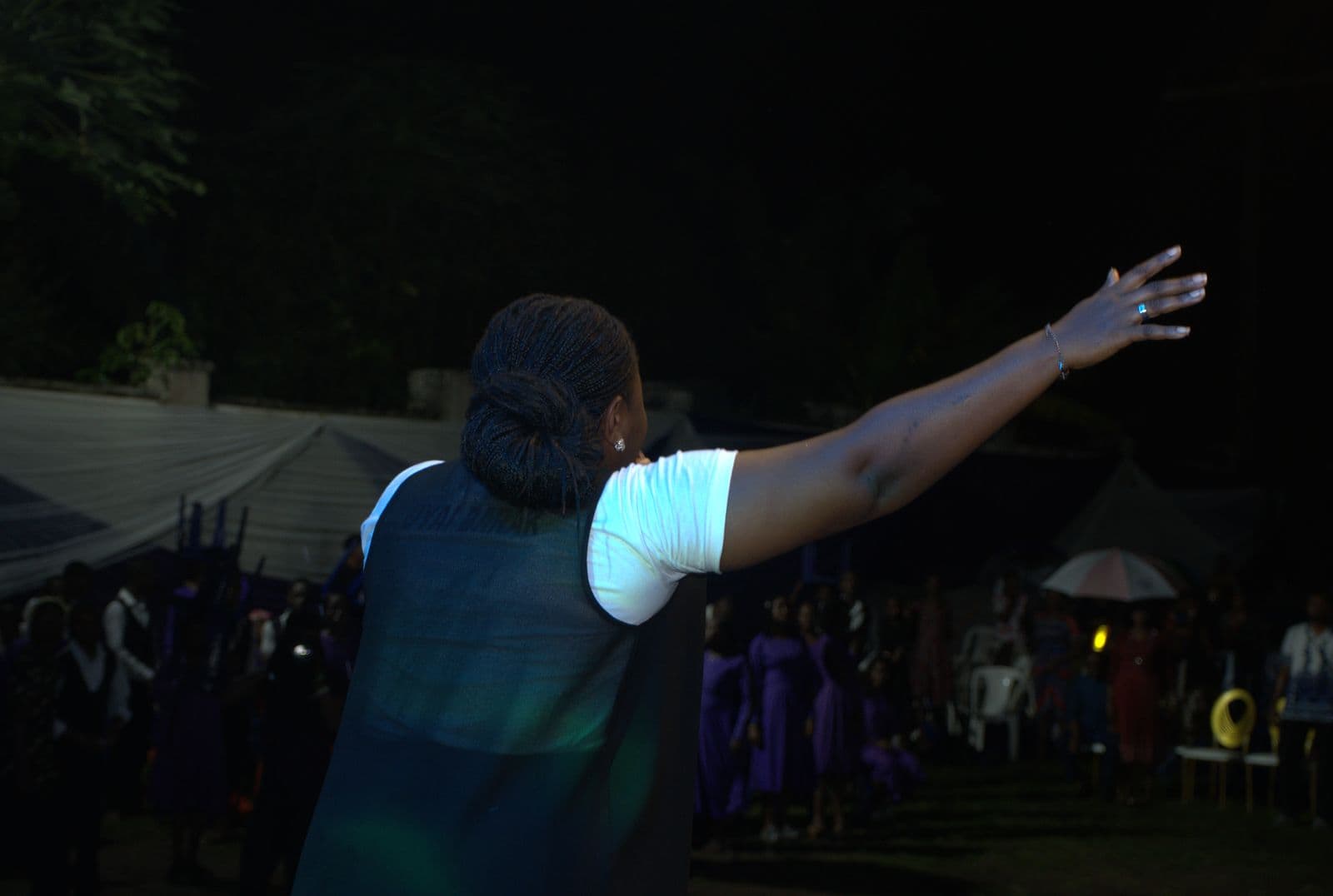 A worshipper with an arm raised, seen from behind at night.