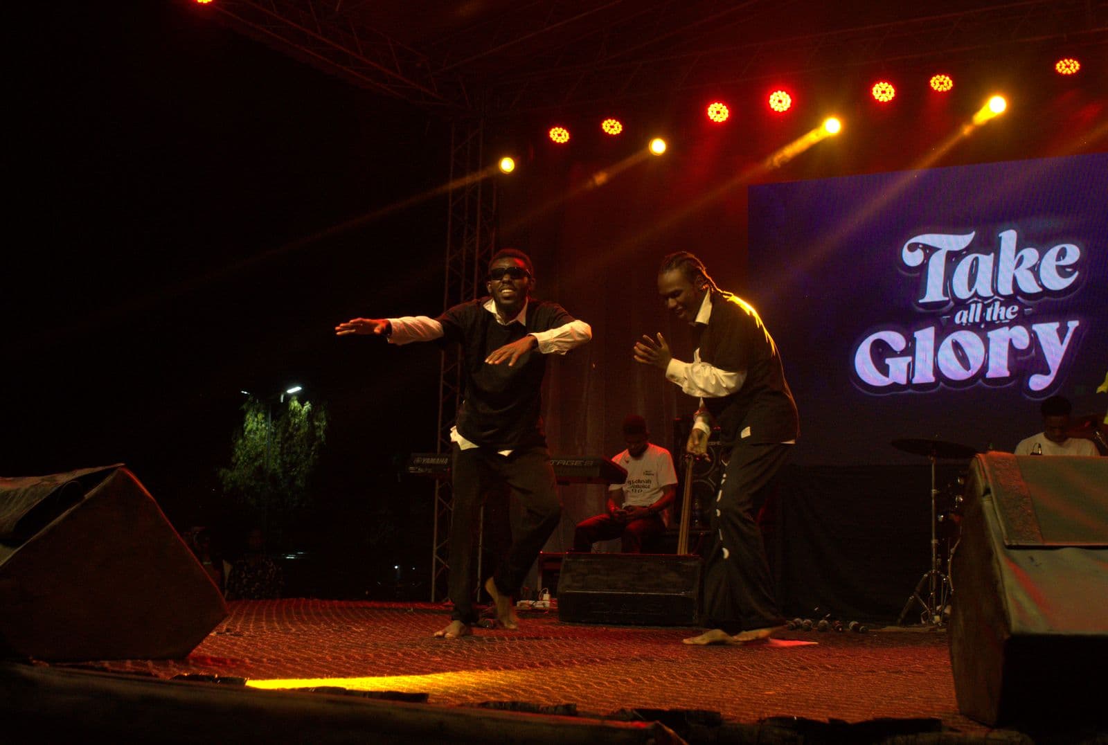 Two performers in a coordinated pose beneath the "Take all the Glory" screen.